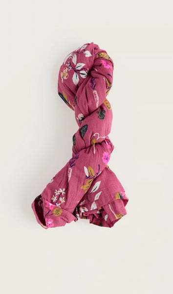 A dusty pink cotton with a colourful floral and butterfly print, styled in a twisted knot on a plain off-white background.