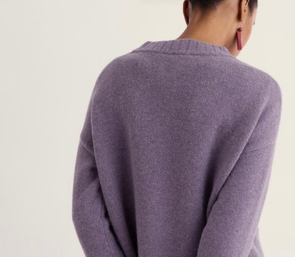 A person shown from the back wearing a soft lavender knit sweater against a plain light background.