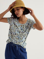 Woman wearing a floral top and straw hat against a plain background.