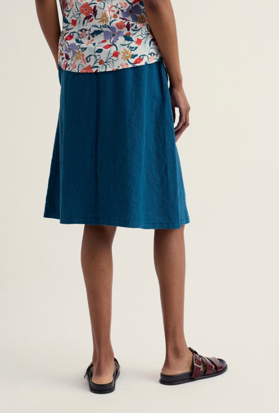 Person wearing a blue skirt and floral top on a plain background.