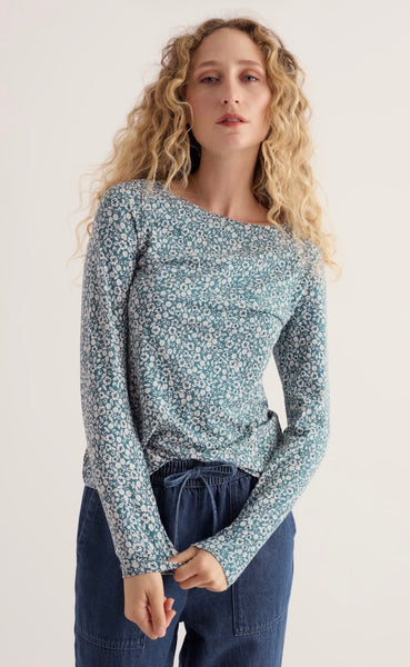 Woman is modelling a Seasalt ditsy pattern top holding cuff of top in her hand. Wearing blue trousers in a studio background.