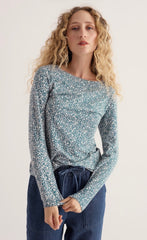 Woman is modelling a Seasalt ditsy pattern top holding cuff of top in her hand. Wearing blue trousers in a studio background.
