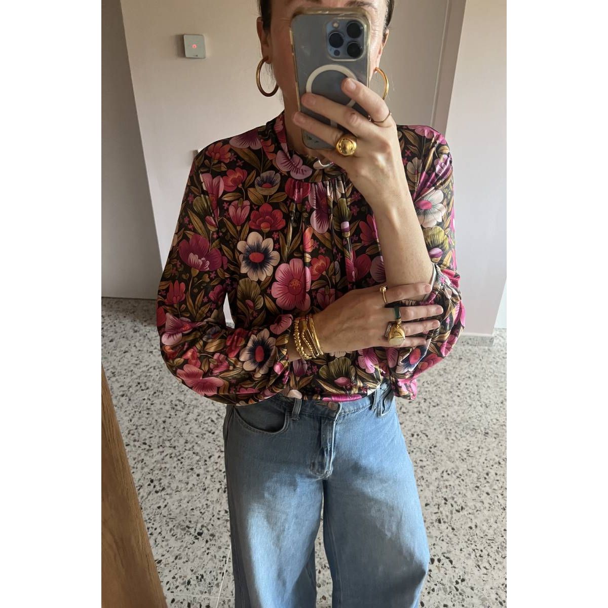 Woman wearing Onjenu Vintage pink floral top with jeans holding phone stood on a speckled floor. 