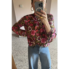 Person wearing a floral blouse and blue jeans taking a mirror selfie.