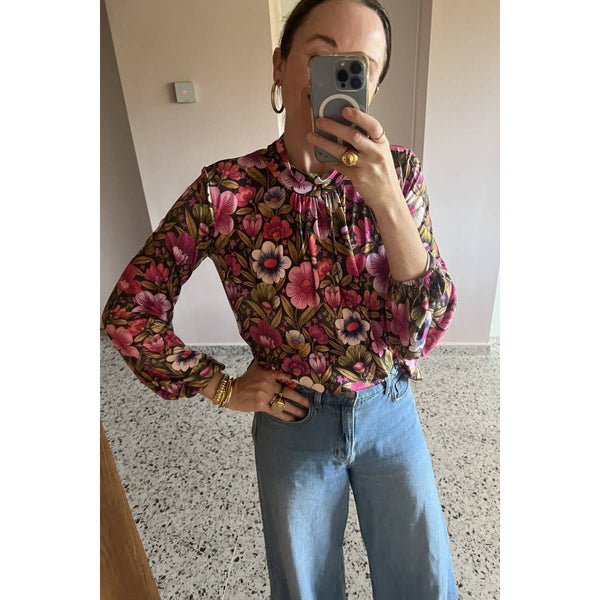 Person wearing a floral blouse and blue jeans taking a mirror selfie.