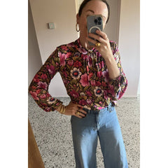 Person wearing a floral blouse and blue jeans taking a mirror selfie.