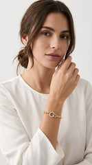 Woman wearing cream blouse modelling Envy gold beaded G diamanté pendant bracelet. Against a studio backdrop. 