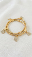 Envy gold wraparound bracelet with heart and circle diamanté charms. On a white fabric background.