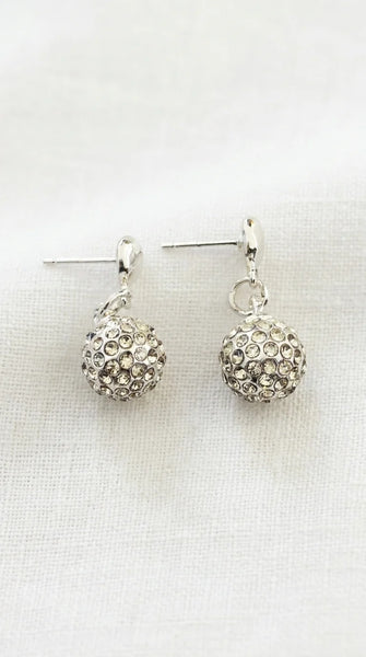 A pair of gold toned dangle earrings with textured, rhinestone-covered round balls, displayed on a white fabric background.
