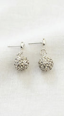 A pair of gold toned dangle earrings with textured, rhinestone-covered round balls, displayed on a white fabric background.