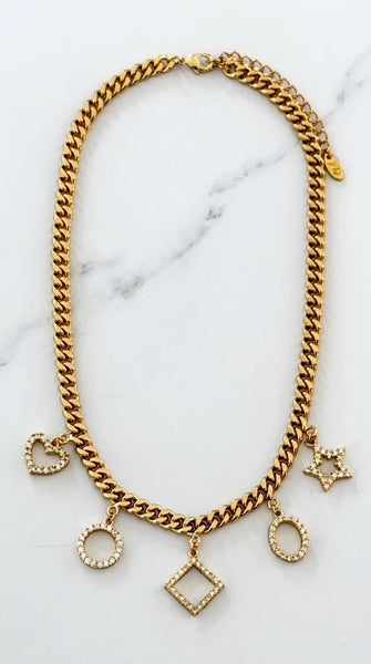 Envy Jewellery gold-toned chunky chain necklace with multiple dangling charms, including hearts, circles, a Star of David, and a diamond-shaped pendant, all embellished with small clear stones, displayed on a white marble background.
