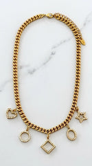 Envy Jewellery gold-toned chunky chain necklace with multiple dangling charms, including hearts, circles, a Star of David, and a diamond-shaped pendant, all embellished with small clear stones, displayed on a white marble background.