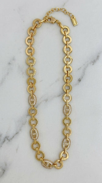 Envy Jewellery gold-tone chain necklace with alternating large oval links and smaller oval links set with clear crystals, displayed on a white marble surface.