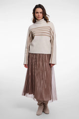 A woman modeling a beige and taupe striped knit turtleneck sweater paired with a pleated taupe midi skirt and beige ankle boots, shot against a seamless light gray studio background.