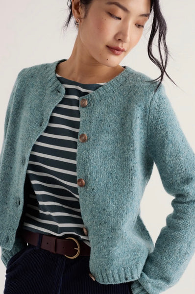 A woman wearing a textured, heathered sage green button-up cardigan over a navy and white striped shirt, paired with a brown belt and dark corduroy trousers, against a plain off-white background.