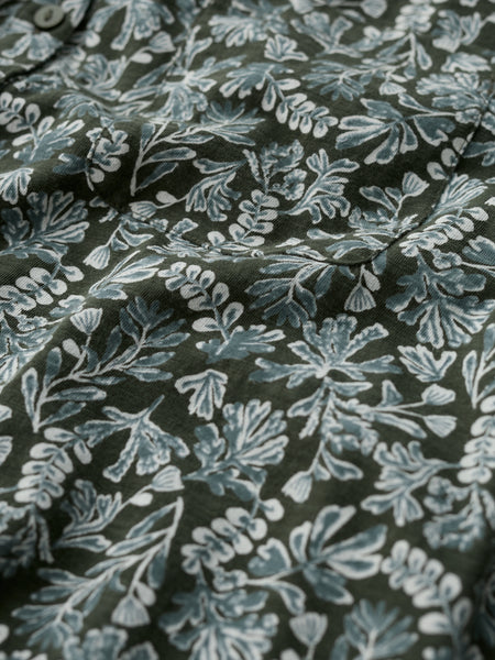 A close-up of a dark olive green fabric with a light blue and white floral block print pattern.