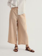 Person wearing beige wide-leg pants and sandals on a plain background.