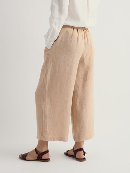 Person wearing beige wide-leg pants and a white top on a plain background.