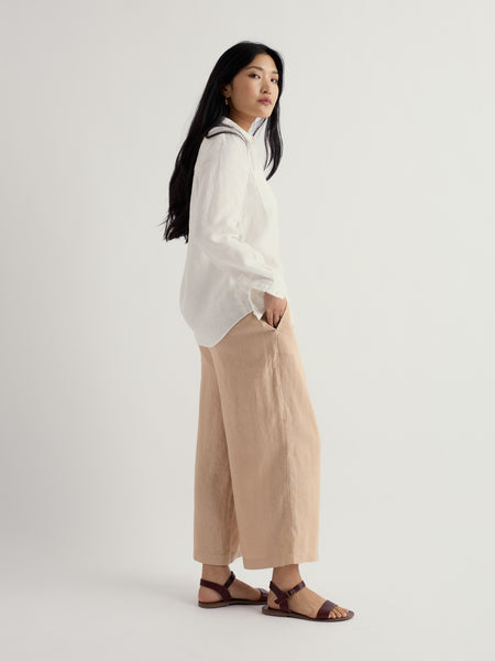 Woman wearing a white blouse and beige pants on a light grey background.