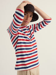 Person wearing a red, white, and blue striped shirt with a black hat on a plain background.