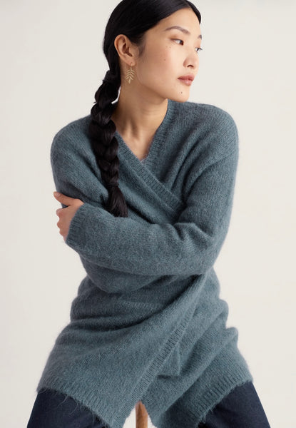A woman wearing a Seasalt, long-open cardigan in a muted slate blue-gray color, posed against a plain off-white studio background.