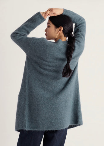A dusty blue open-front cardigan sweater with long sleeves and two front patch pockets, displayed flat against a light off-white background.