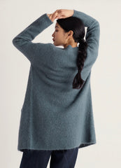 A woman wearing a Seasalt, oversized long-sleeve sweater in a muted slate blue-gray color, shown from the back against a plain light background.