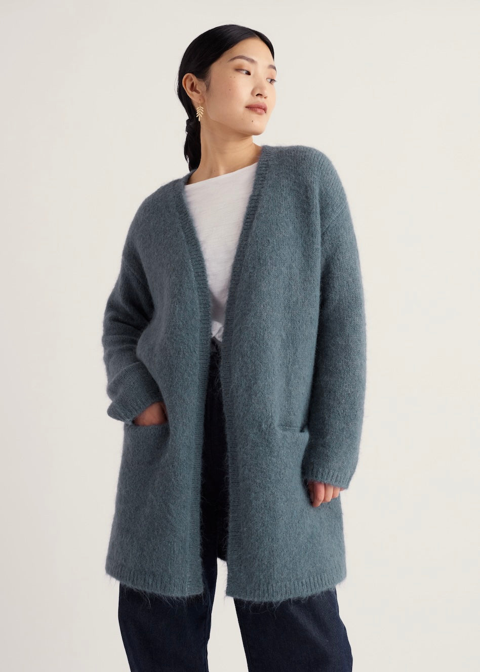 A woman wearing a Seasalt open-front long cardigan in a muted blue-gray color, styled over a white top and dark pants, set against a plain light background.