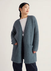 A woman wearing a Seasalt open-front long cardigan in a muted blue-gray color, styled over a white top and dark pants, set against a plain light background.