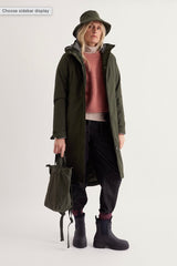 A model wearing a Seasalt olive green hooded parka coat, a dusty pink knit sweater, black pants, and black boots, holding an olive green canvas bag. The image is set against a plain light gray studio background with a text overlay in the top left corner that reads 'Choose sidebar display'.
