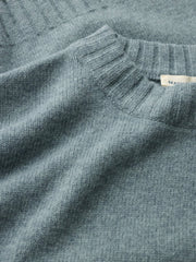 Close-up of a Seasalt knit sweater in a muted dusty blue-gray color, showing the texture of the fabric and a small white brand tag near the collar.