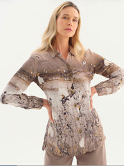 A woman modeling a long-sleeve Dolcezza button-up shirt with an abstract paint-splatter print in beige, brown, white, and black, paired with beige trousers against a plain white studio background.