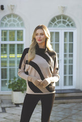 A woman wearing a beige and black Diagonal pattern Pomodoro knit sweater and matching beige gloves, standing outdoors in front of a white building with arched windows.
